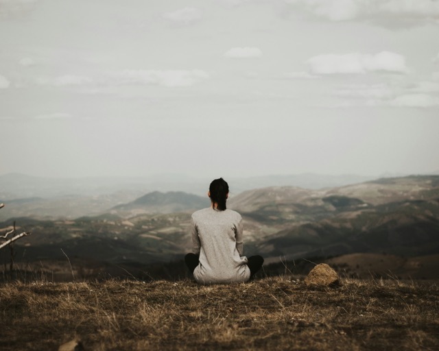 A woman practices mindfulness mediation looking over rolling hills and mountains. 