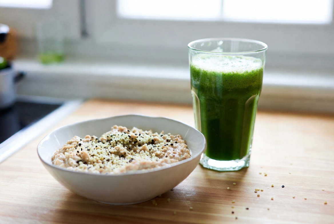 A breakfast bowl topped with hemp seeds beside a green smoothie in a bright kitchen. 