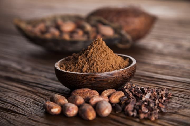 Raw cacao nibs and powder surrounded by other wholesome superfood ingredients on wood. 