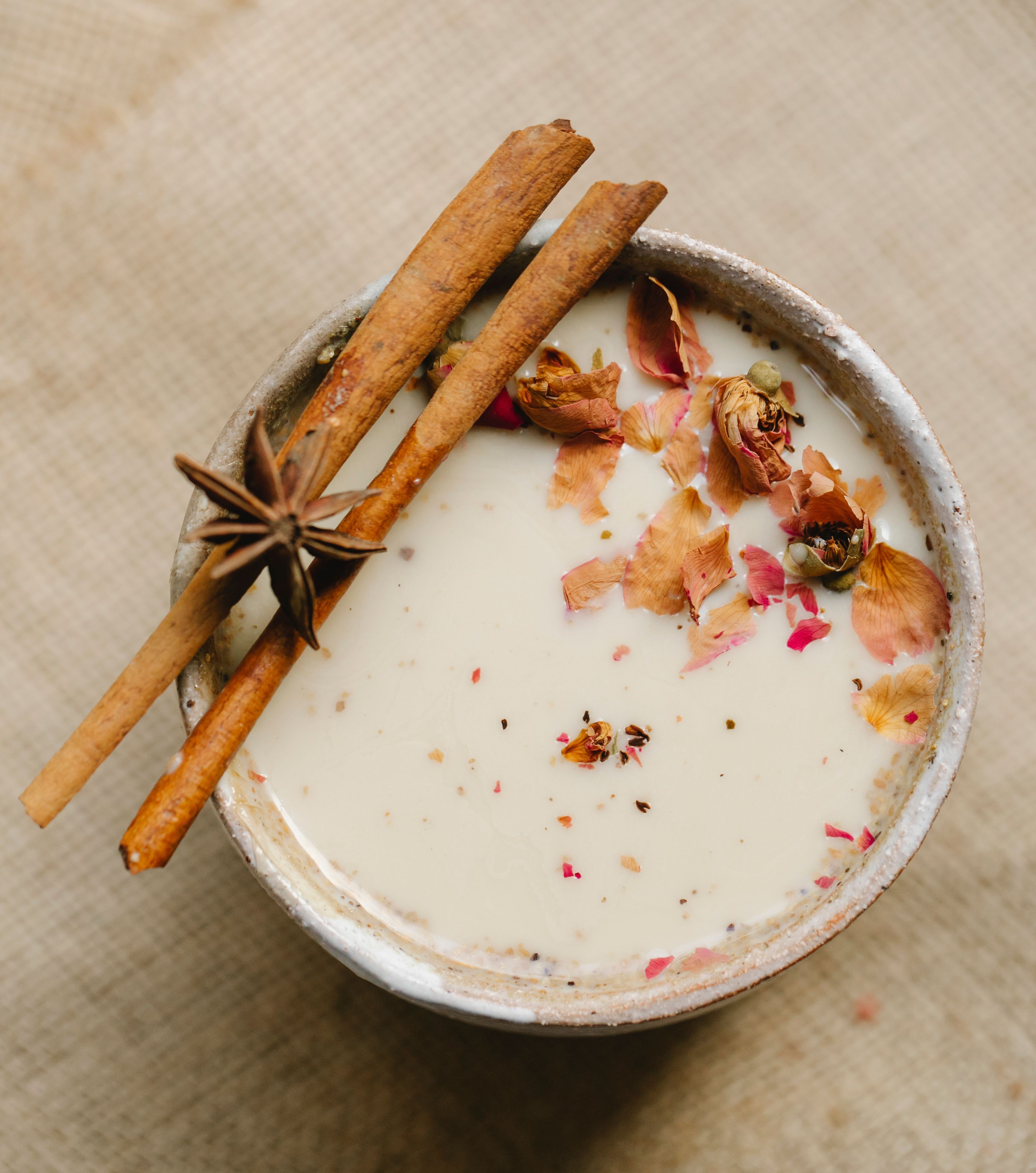 Small daily choices — a warm cup in the evening — are where steadiness actually gets built. A warm cup of ashwagandha moon-milk latte with ashwagandha sticks resting on the rim and garnished with dried warm spices.
